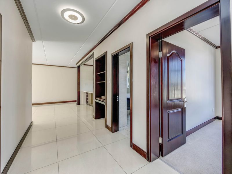 A bright, spacious hallway featuring polished tile flooring, dark wood trim, and built-in shelving, providing access to adjacent rooms.