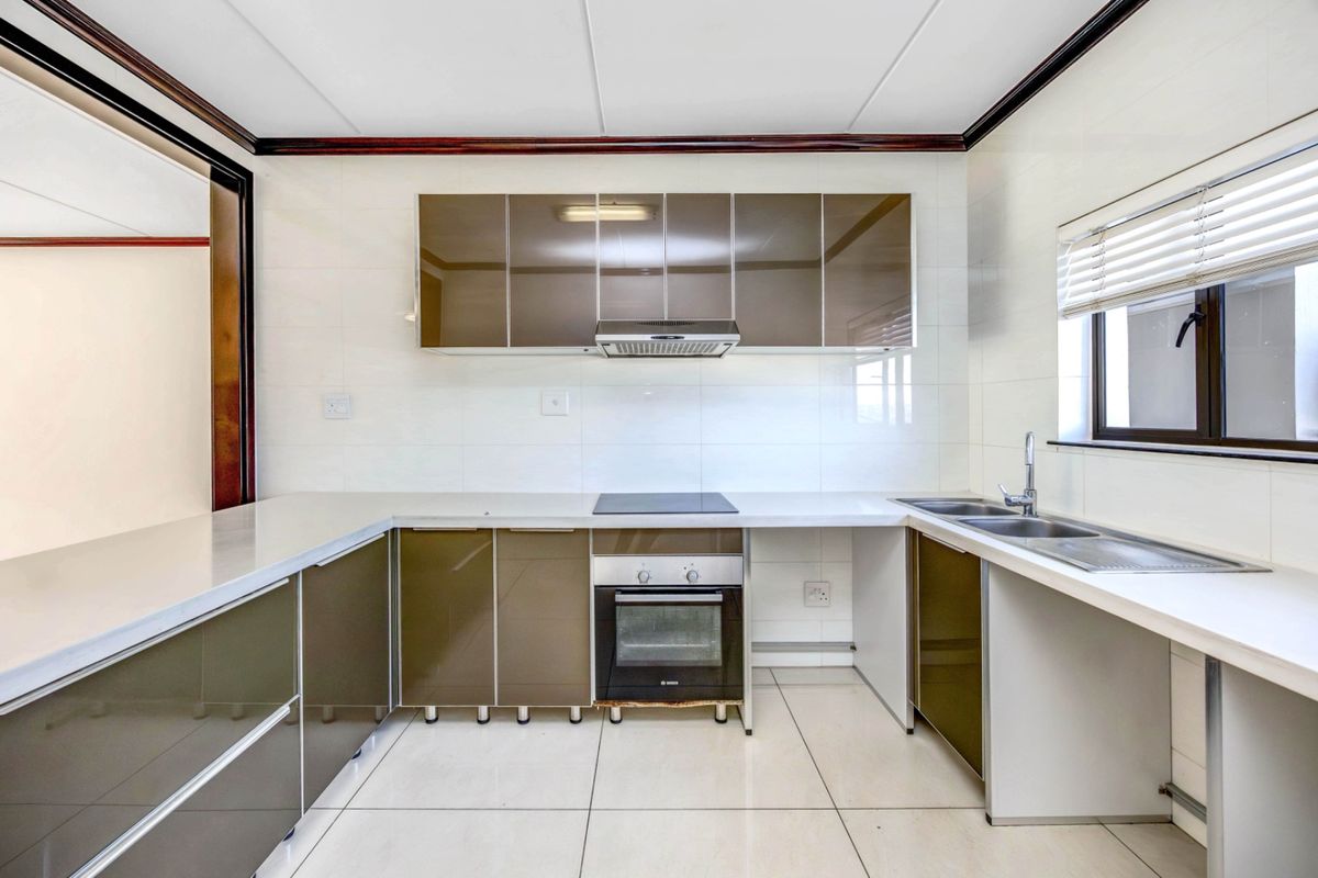 A clean, modern kitchen featuring high-gloss cabinetry, integrated oven and hob, double sink, and neutral tiled finishes throughout.