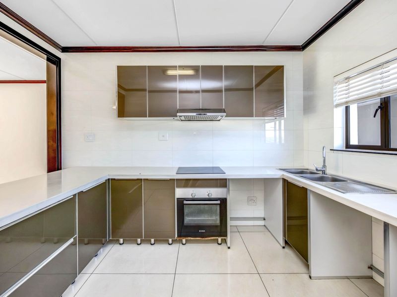 A clean, modern kitchen featuring high-gloss cabinetry, integrated oven and hob, double sink, and neutral tiled finishes throughout.