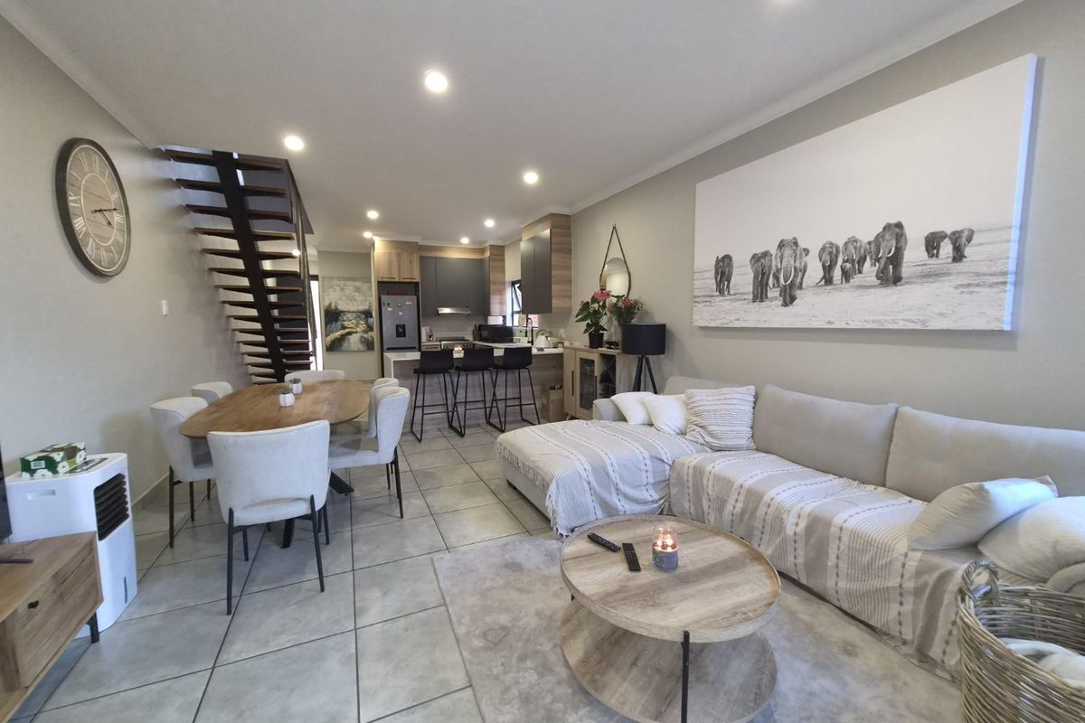 Spacious open-plan living and dining area featuring a modern kitchen with island, tiled flooring, and a feature staircase.