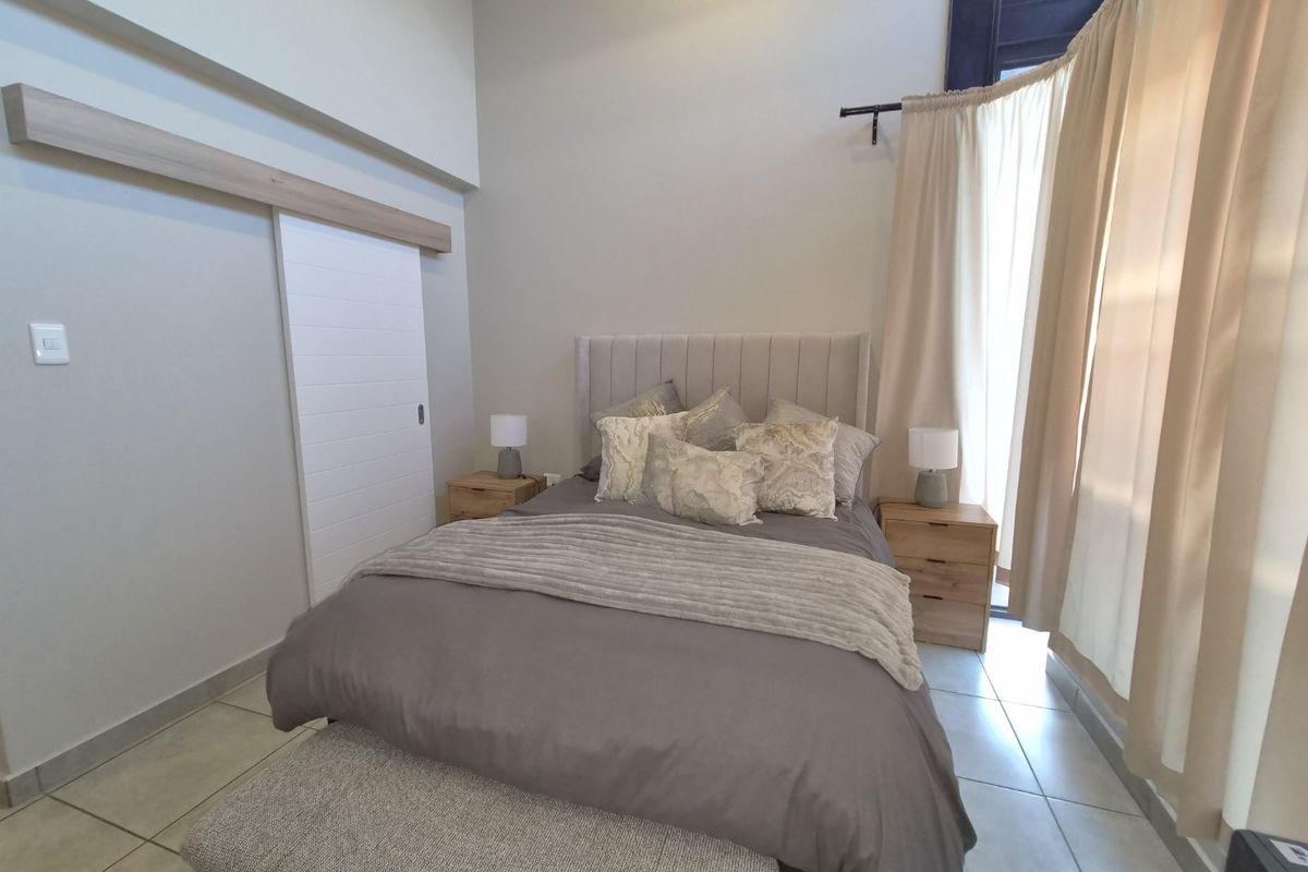 A well-lit bedroom featuring tiled flooring, a high ceiling, and a modern sliding door, creating a bright and comfortable living space.