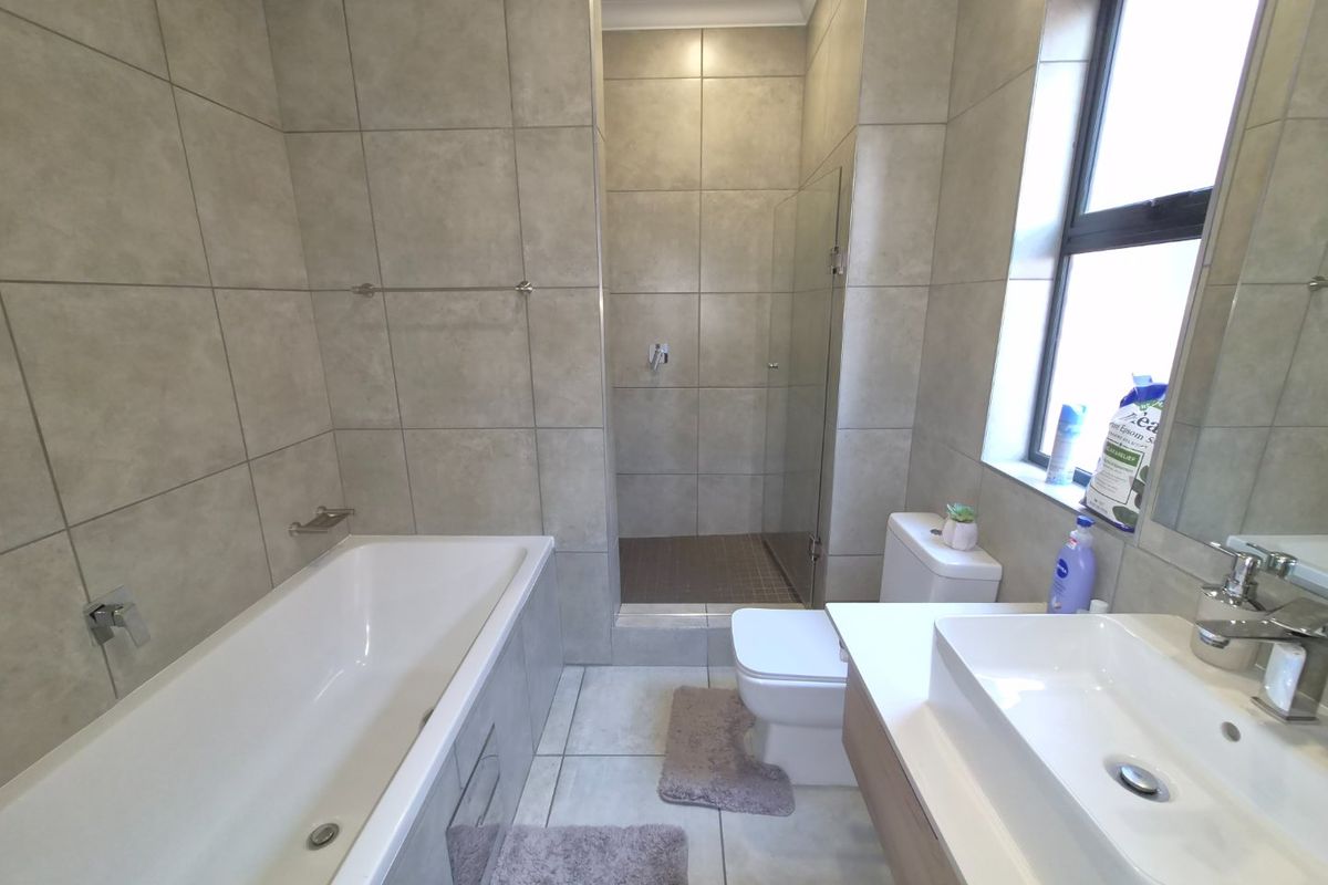 Modern bathroom featuring a built-in bathtub, separate walk-in shower with glass screen, wall-mounted vanity with basin, and neutral floor-to-ceiling tiling.