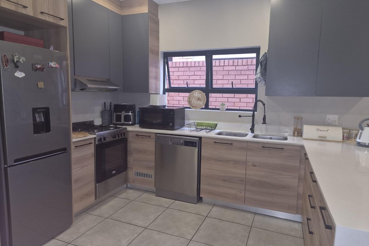 Modern kitchen featuring wood-grain and grey cabinetry, stone countertops, integrated appliances, and a double basin sink with a contemporary mixer tap.