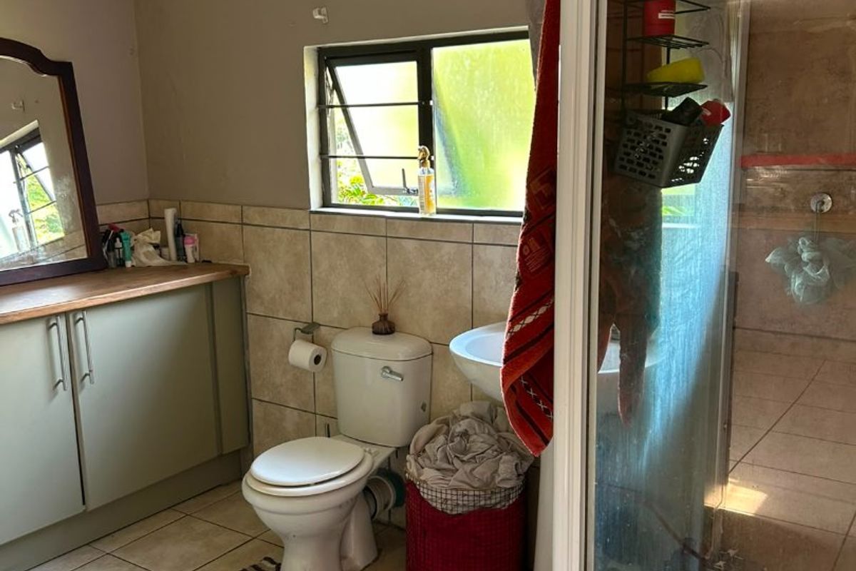 A functional bathroom featuring a vanity cabinet, pedestal basin, toilet, and a glass-enclosed shower with tiled finishes.