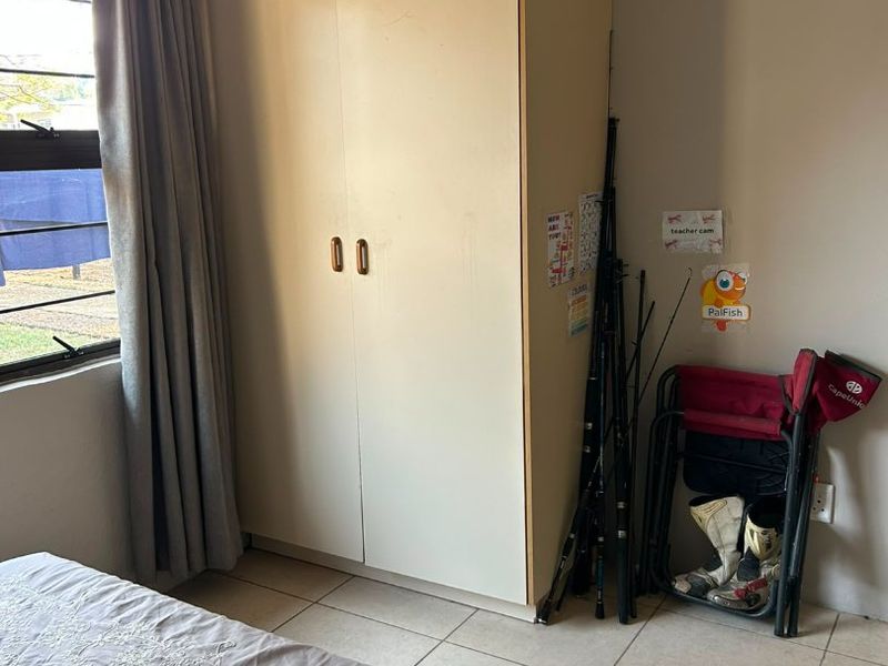 A bedroom featuring a built-in wardrobe, tiled flooring, and a window with neutral curtains.