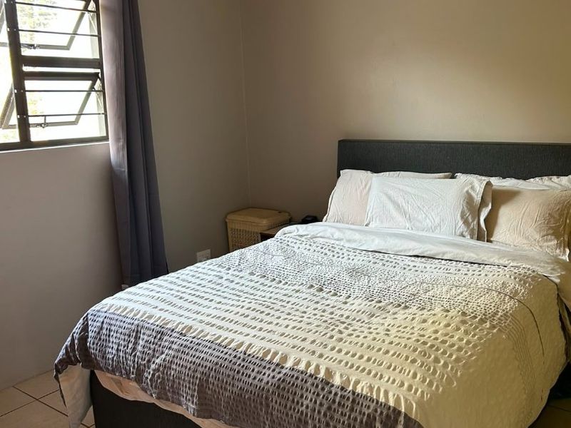 A functional bedroom featuring tiled flooring and a louvered window, providing a neutral space ready for personalization.