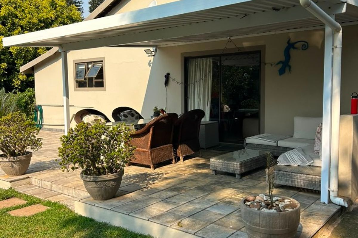 A well-maintained covered patio featuring paved flooring and direct access to the interior through a sliding glass door, overlooking a private garden area.