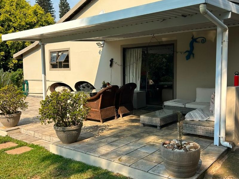 A well-maintained covered patio featuring paved flooring and direct access to the interior through a sliding glass door, overlooking a private garden area.