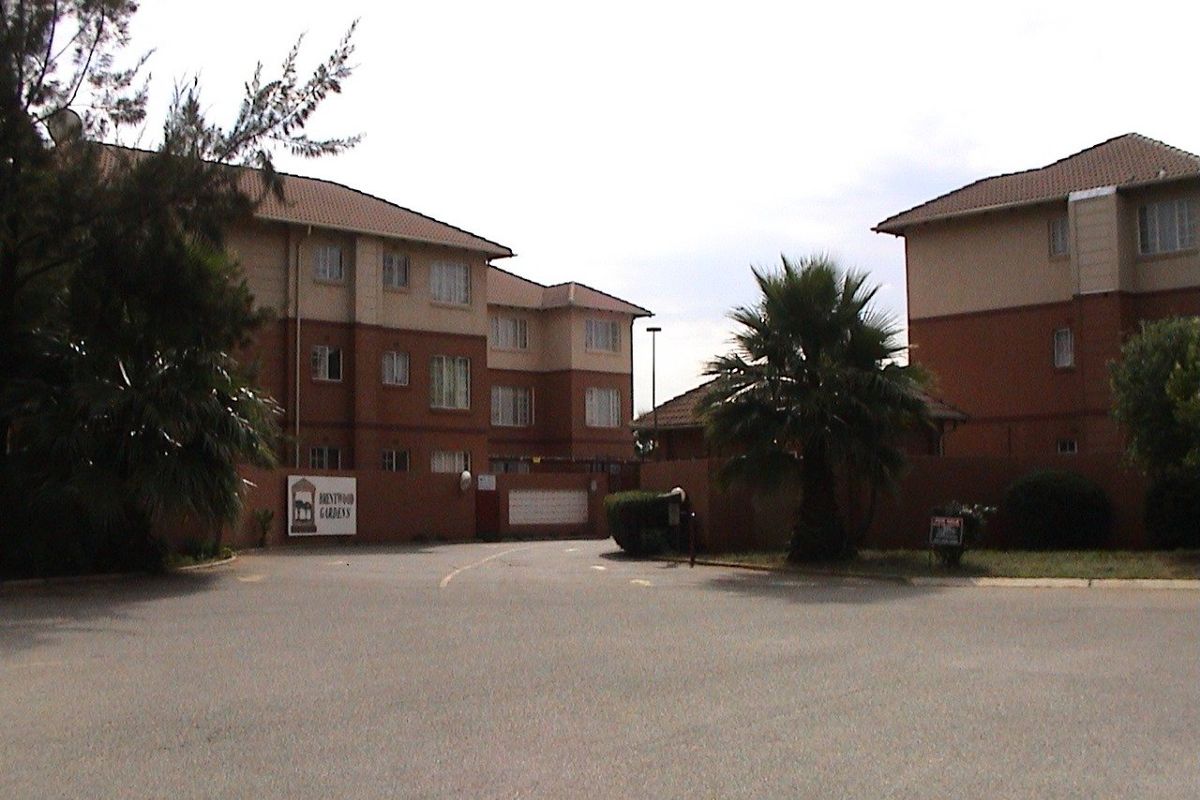 Front view of the Brentwood Gardens apartment complex, featuring multi-story brick buildings, a secure gated entrance, and paved driveway access.