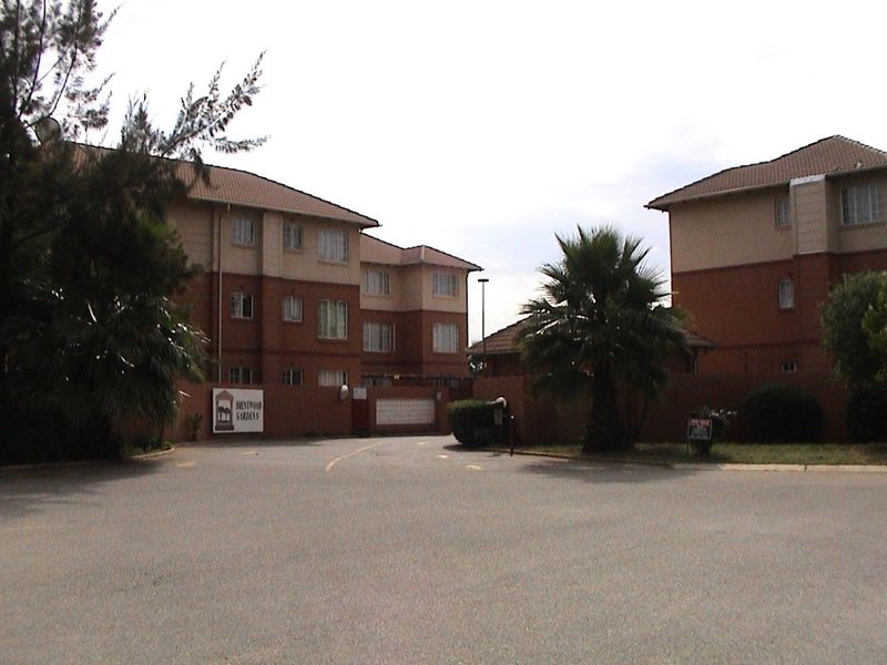 Front view of the Brentwood Gardens apartment complex, featuring multi-story brick buildings, a secure gated entrance, and paved driveway access.
