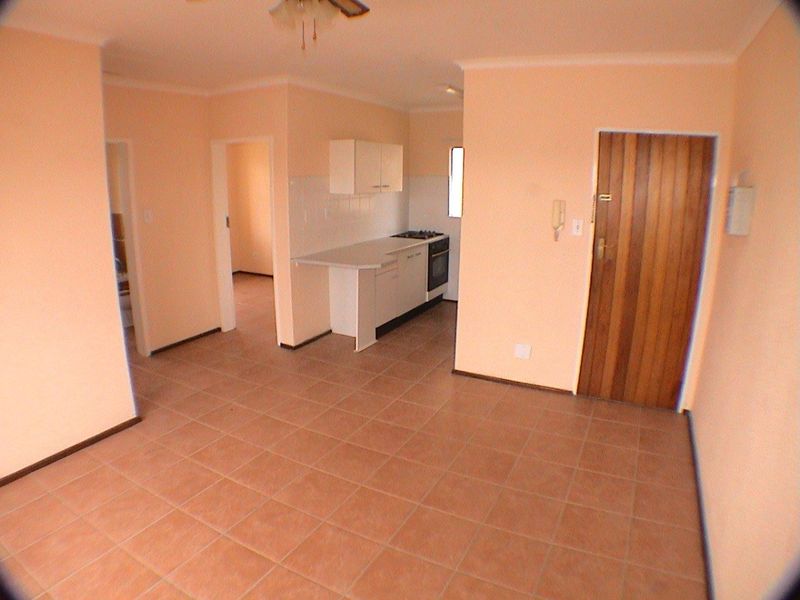An open-plan living and kitchen area featuring tiled flooring, built-in cabinetry, and a functional kitchen layout in a neutral setting.