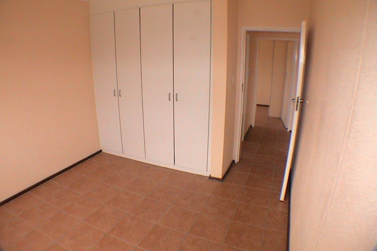 An empty bedroom featuring built-in cupboards and tiled flooring, providing a neutral space ready for personalization.