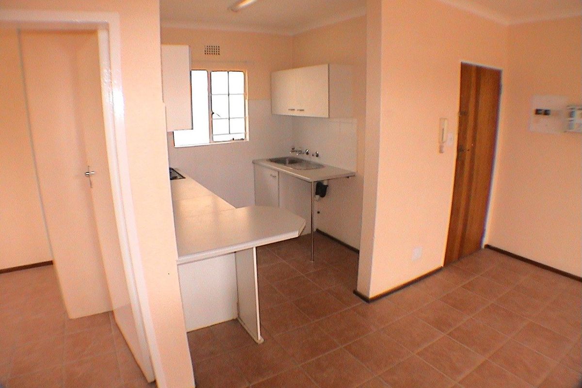 A compact, empty kitchen featuring basic built-in cabinetry, a stainless steel sink, and tiled flooring, offering a functional space ready for modernization.