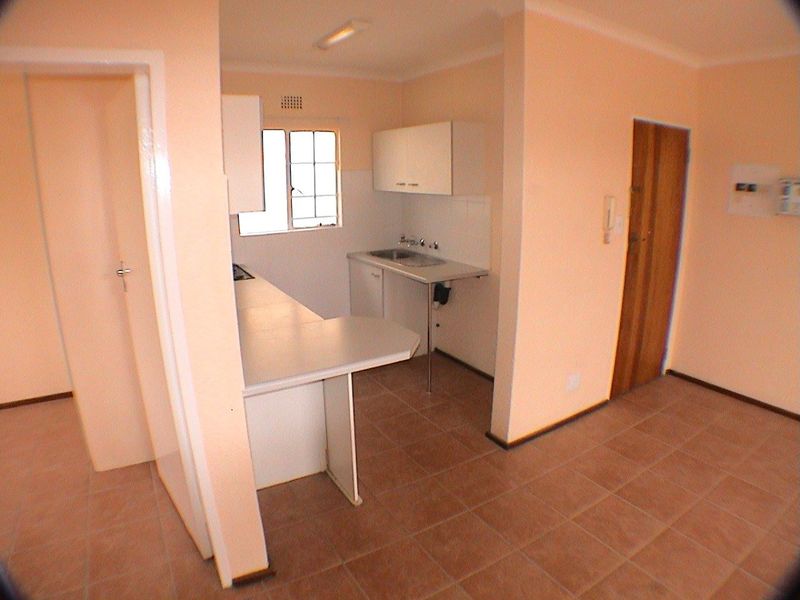 A compact, empty kitchen featuring basic built-in cabinetry, a stainless steel sink, and tiled flooring, offering a functional space ready for modernization.