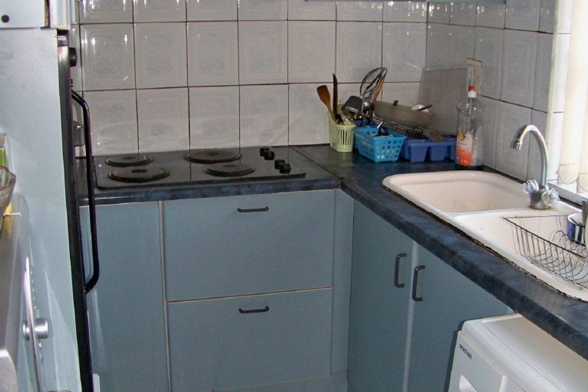 Compact kitchen featuring blue cabinetry, laminate countertops, an electric hob with extractor fan, and tiled finishes throughout.