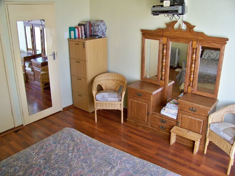 A bedroom featuring laminate flooring and a mirrored door, providing a functional space with neutral wall finishes.