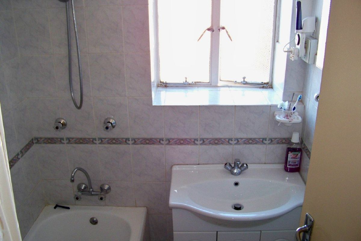 Compact bathroom featuring a bathtub with shower mixer, vanity basin with storage cabinet, and tiled wall finishes.