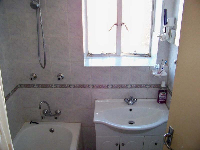 Compact bathroom featuring a bathtub with shower mixer, vanity basin with storage cabinet, and tiled wall finishes.