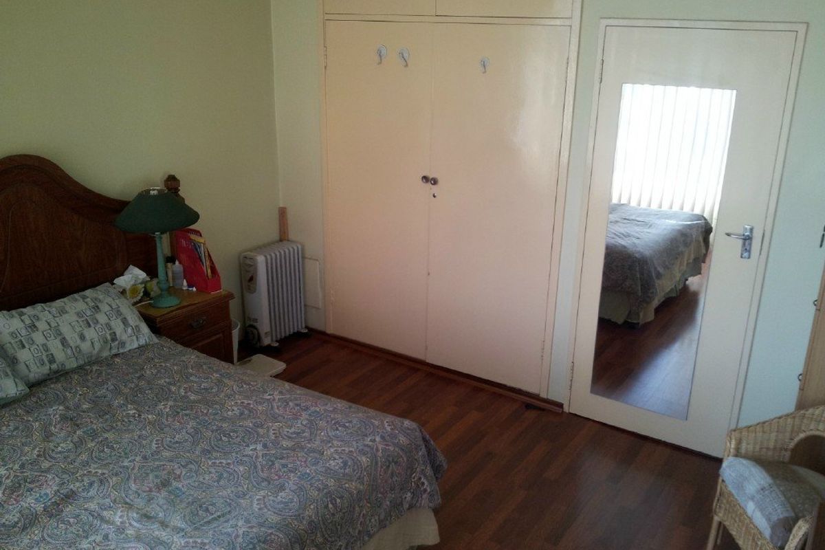 A bedroom featuring laminate flooring and built-in cupboards with a mirrored door.