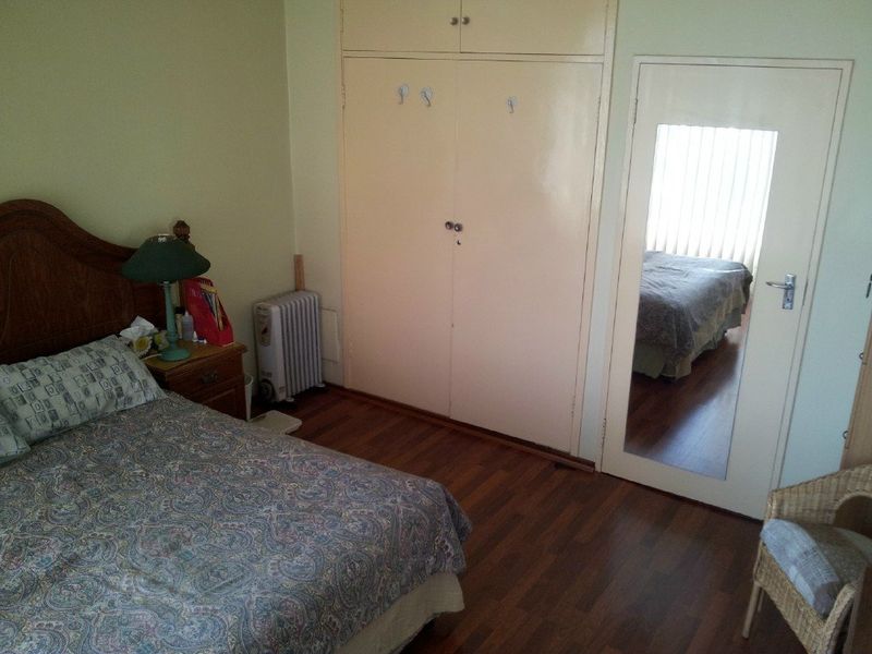 A bedroom featuring laminate flooring and built-in cupboards with a mirrored door.