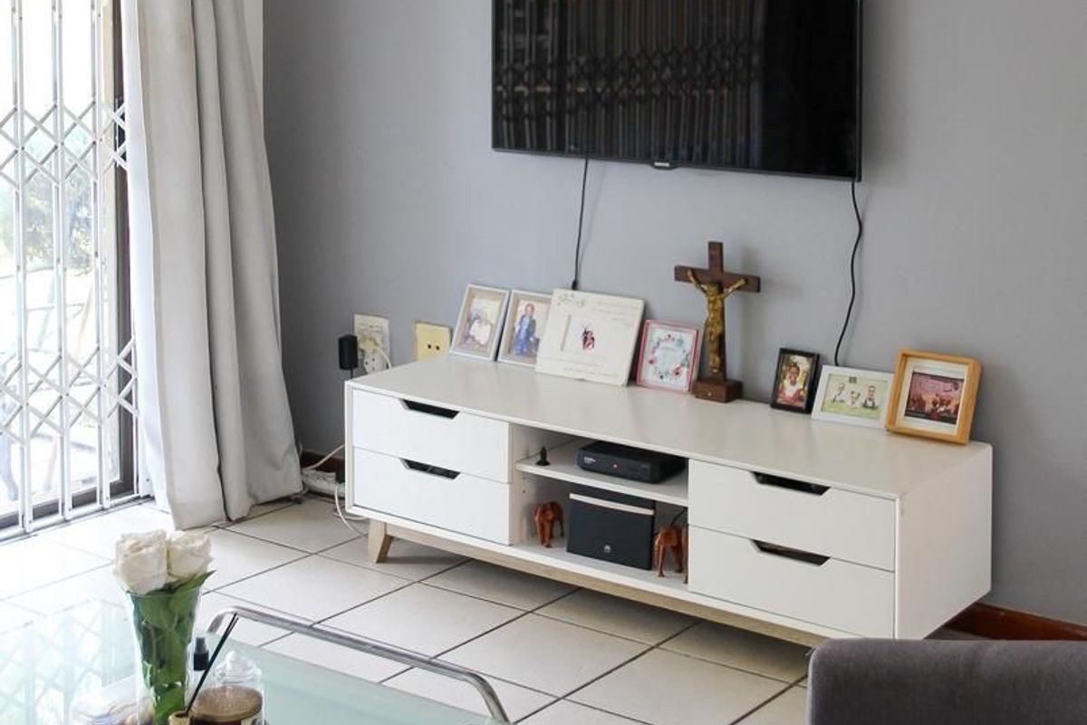 A well-maintained living room featuring tiled flooring and a sliding door with a security gate, providing access to the outdoor area.