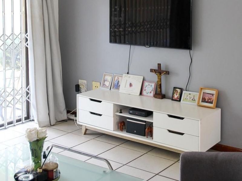 A well-maintained living room featuring tiled flooring and a sliding door with a security gate, providing access to the outdoor area.