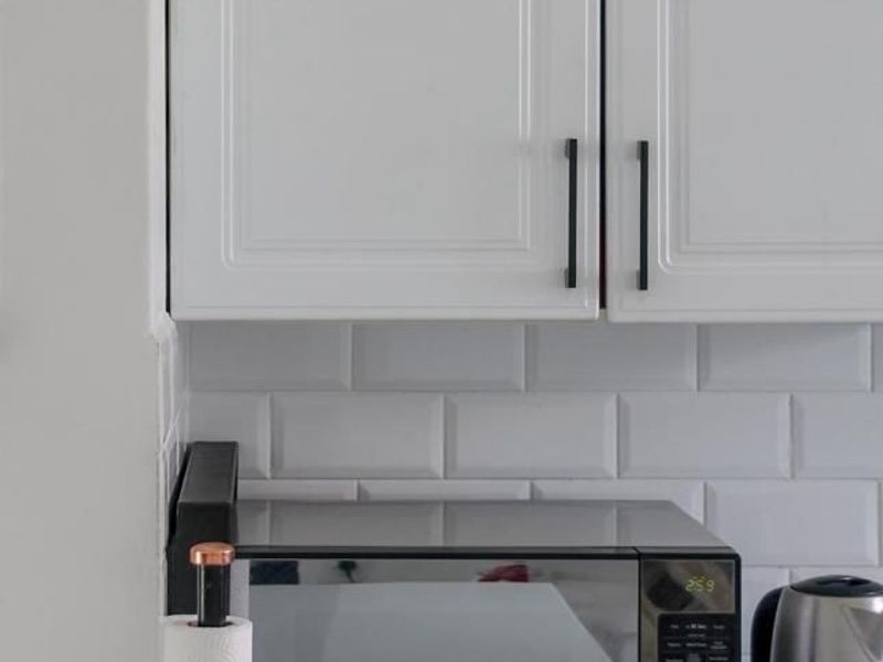 A clean, modern kitchen area featuring white shaker-style cabinetry, a classic subway tile backsplash, and a smooth quartz countertop.