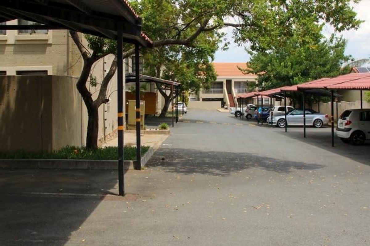 A view of the apartment complex parking area featuring covered parking bays and mature trees.