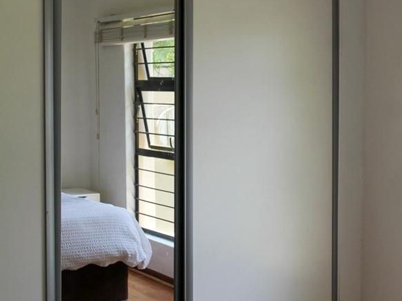 A bedroom featuring a large built-in mirrored sliding wardrobe, laminate flooring, and a functional louvre window providing natural light.