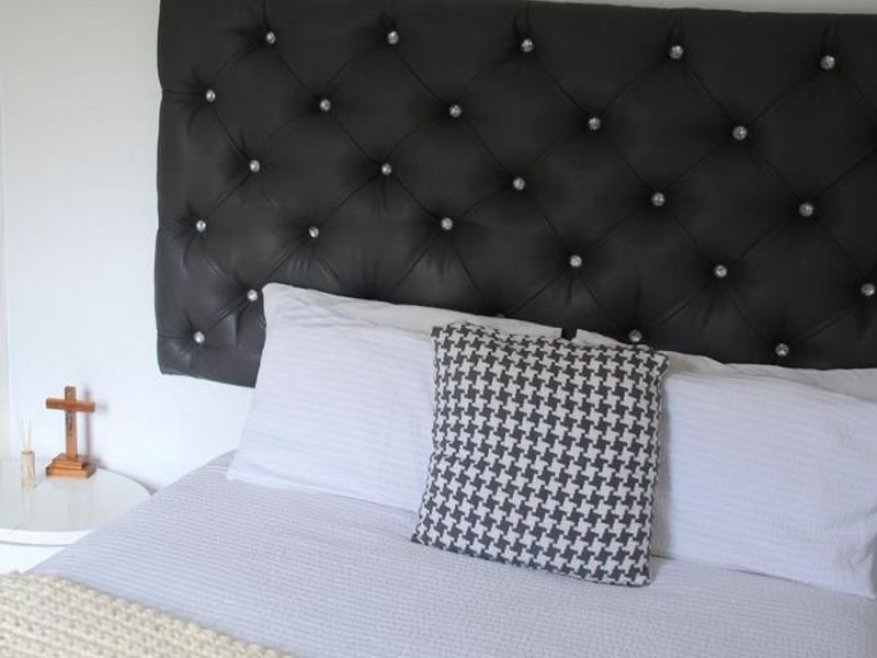 A close-up view of a bedroom featuring a tufted black leather headboard with decorative crystal buttons.