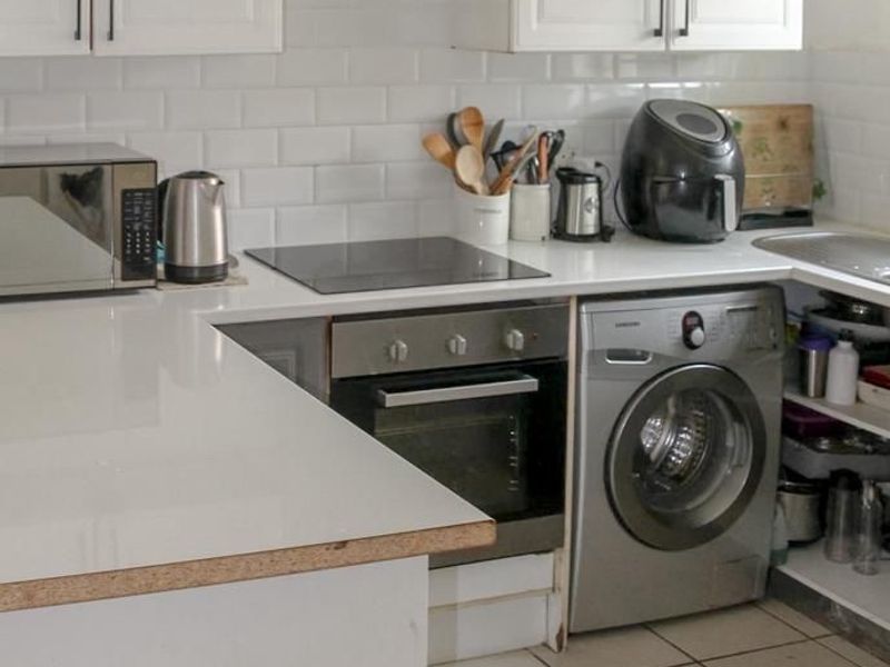 Compact kitchen featuring white cabinetry, subway tile backsplash, built-in oven, electric cooktop, and tiled flooring.