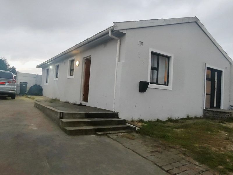 Front exterior view of a single-story house featuring a concrete driveway, entrance steps, and perimeter boundary walling.