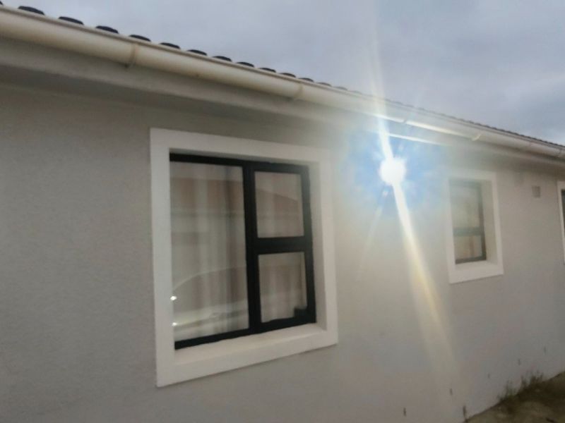A view of the rear exterior elevation featuring modern aluminium window frames, guttering, and exterior wall lighting along a paved walkway.