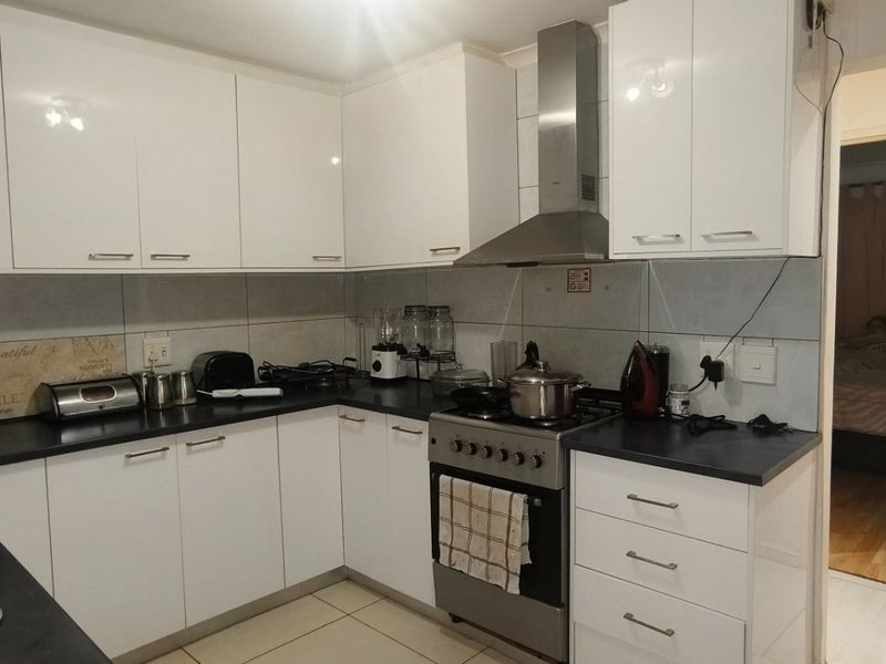 A functional kitchen featuring white gloss cabinetry, a stainless steel freestanding stove with extractor fan, and a double bowl sink with tiled splashback.