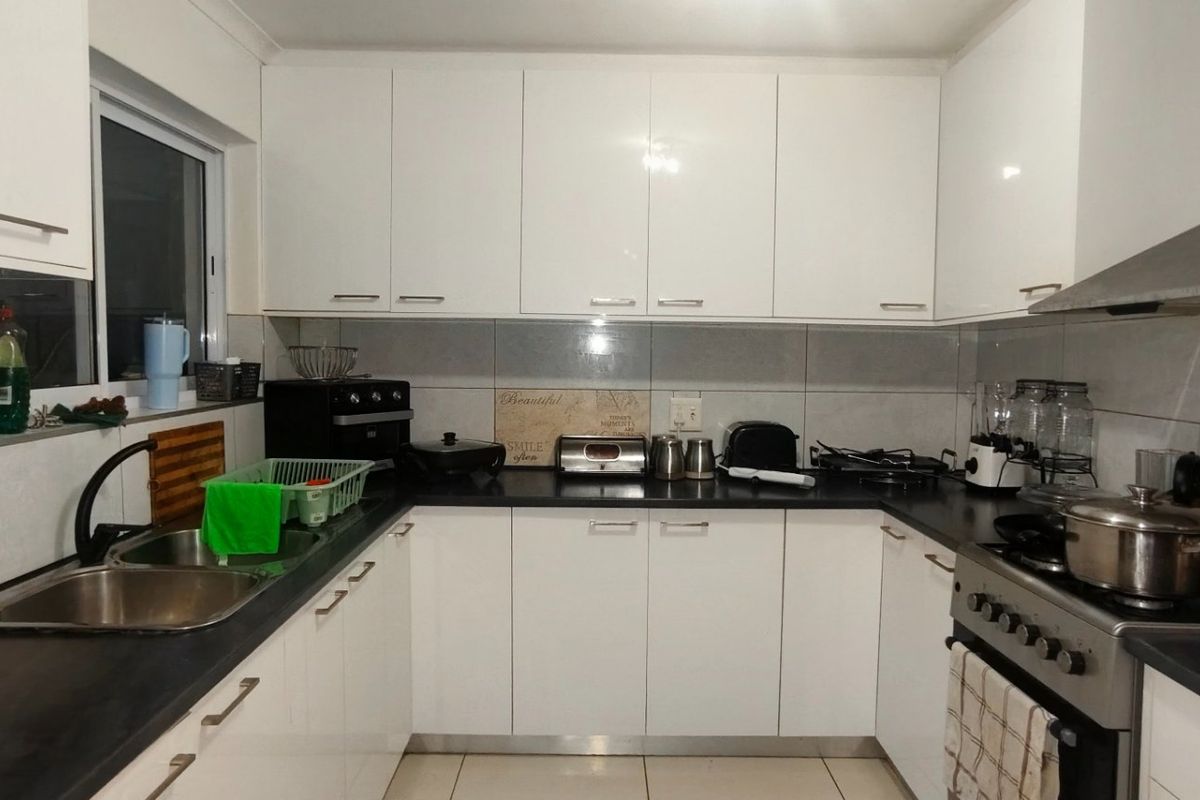 A functional U-shaped kitchen featuring white gloss cabinetry, dark countertops, tiled backsplash, and a stainless steel gas stove with an extractor fan.