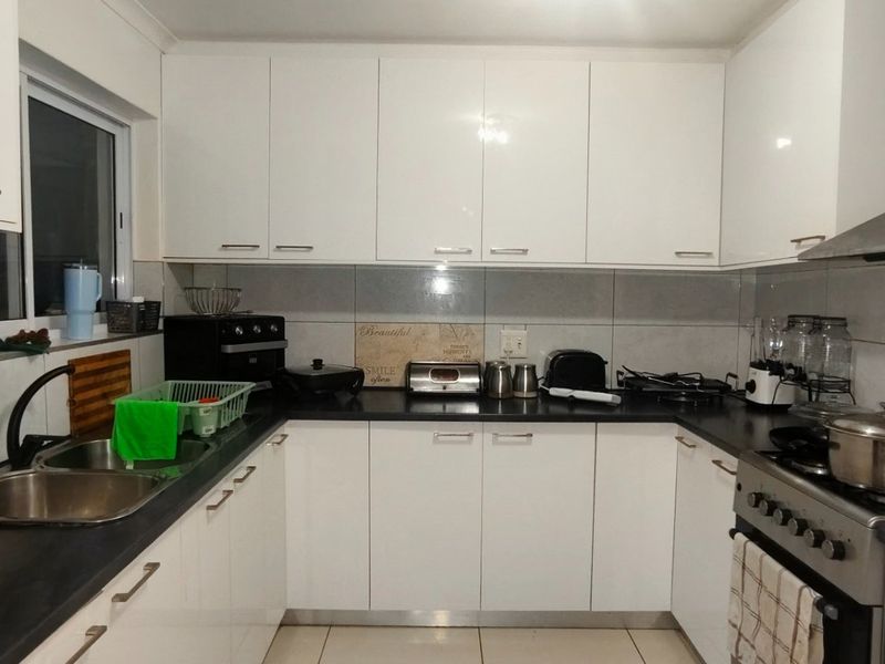 A functional U-shaped kitchen featuring white gloss cabinetry, dark countertops, tiled backsplash, and a stainless steel gas stove with an extractor fan.