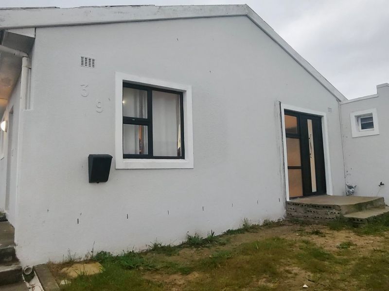 Front elevation of a single-story house featuring a painted facade, aluminium window frames, and concrete entrance steps leading to the main doorway.