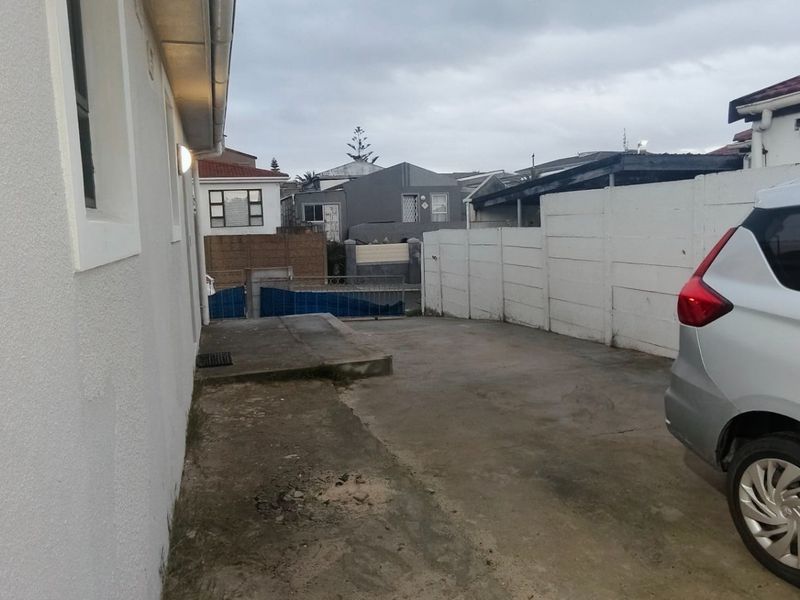 A view of the rear exterior area featuring a concrete driveway and boundary walling.