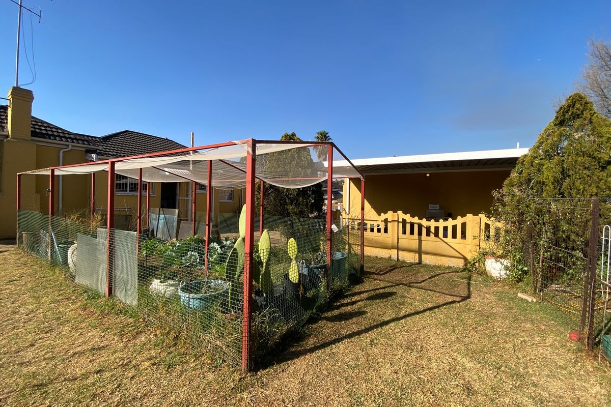 Rear garden area featuring a metal-framed vegetable enclosure, a covered patio space, and established lawn, offering potential for landscaping improvements.