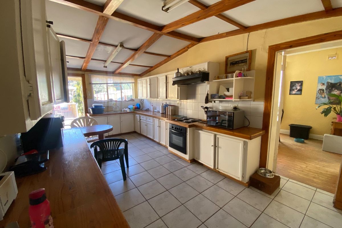 A dated kitchen featuring exposed timber ceiling beams, tiled flooring, built-in cabinetry, and a built-in oven with an extractor fan.