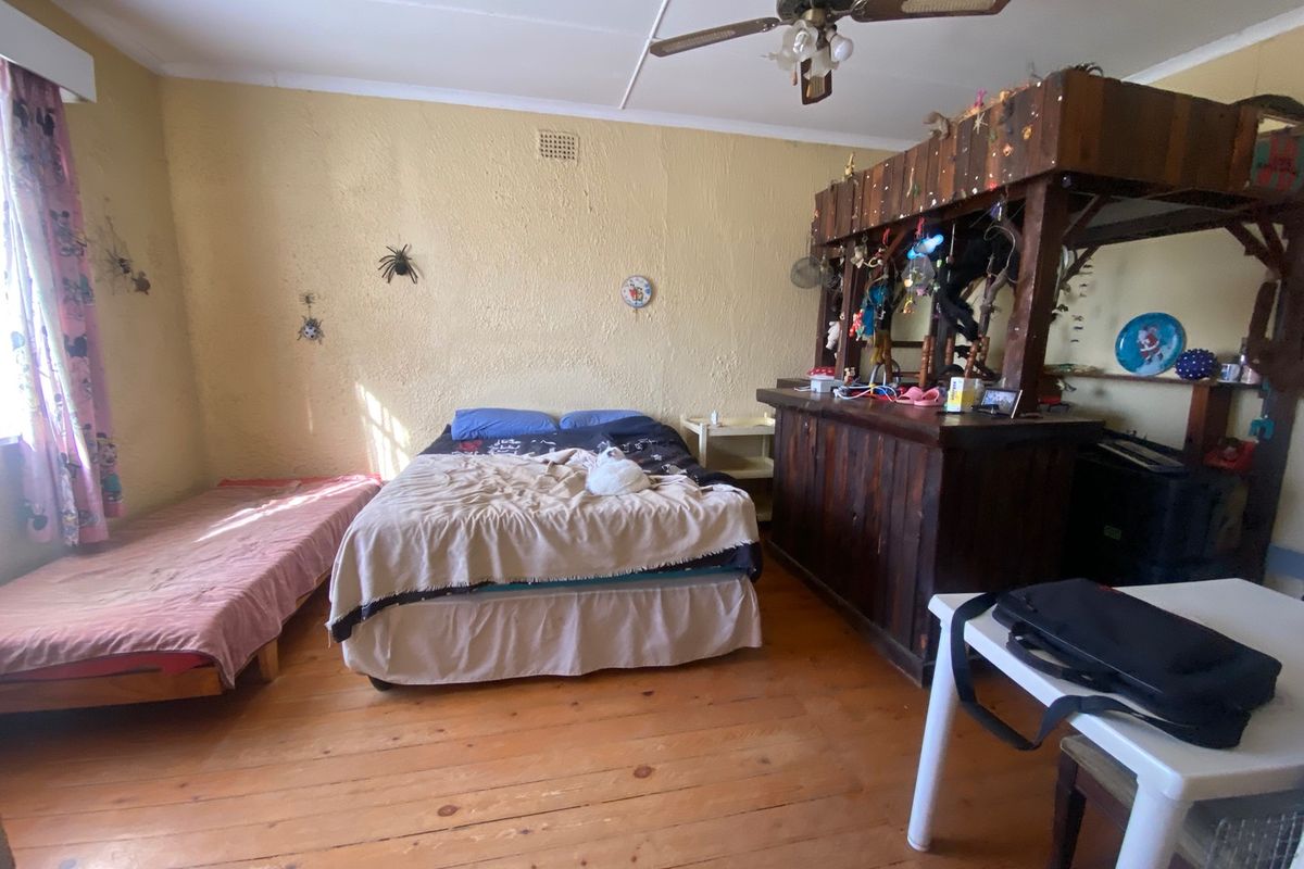 A bedroom featuring timber flooring and a ceiling fan, requiring cosmetic updates to the wall finishes to improve the overall aesthetic.
