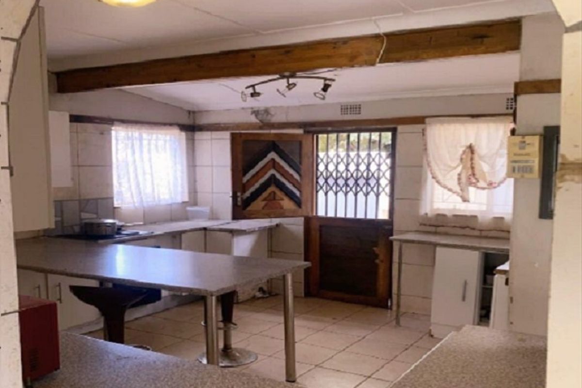 A dated kitchen featuring tiled flooring, exposed timber ceiling beams, and built-in cabinetry with laminate countertops, requiring cosmetic updates to modernize the space.