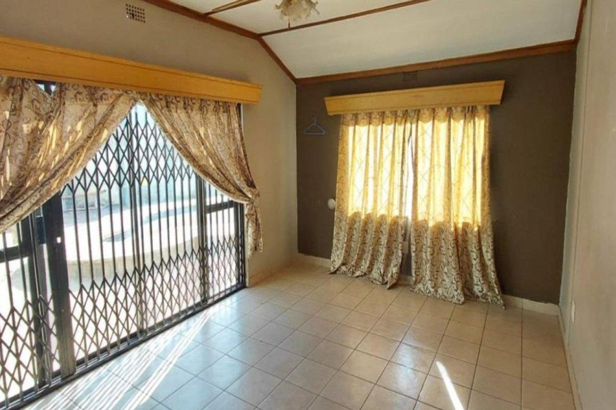 An empty living room featuring tiled flooring, a vaulted ceiling, and security gates over the windows.