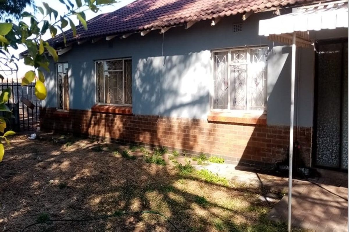 Rear view of the house featuring a brick and painted facade, tiled roof, and a paved patio area with security bars on windows.