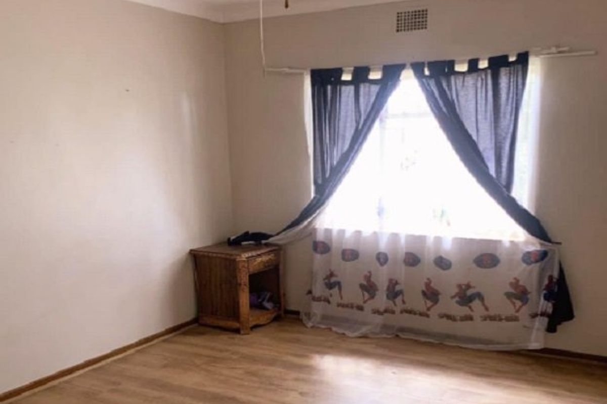 A simple, vacant bedroom featuring laminate flooring, a ceiling fan, and a window with curtain fixtures.
