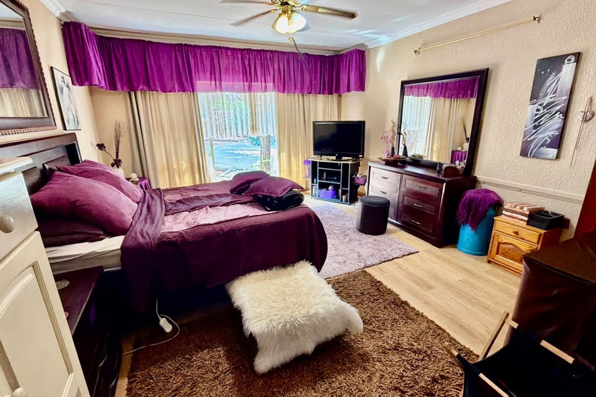 A spacious bedroom featuring laminate flooring, a ceiling fan, and a sliding glass door providing natural light and garden access.