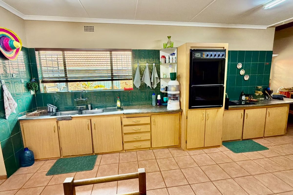 A functional kitchen featuring wooden cabinetry, a double sink, built-in double oven, and green tiled splashbacks with ceramic floor tiles.