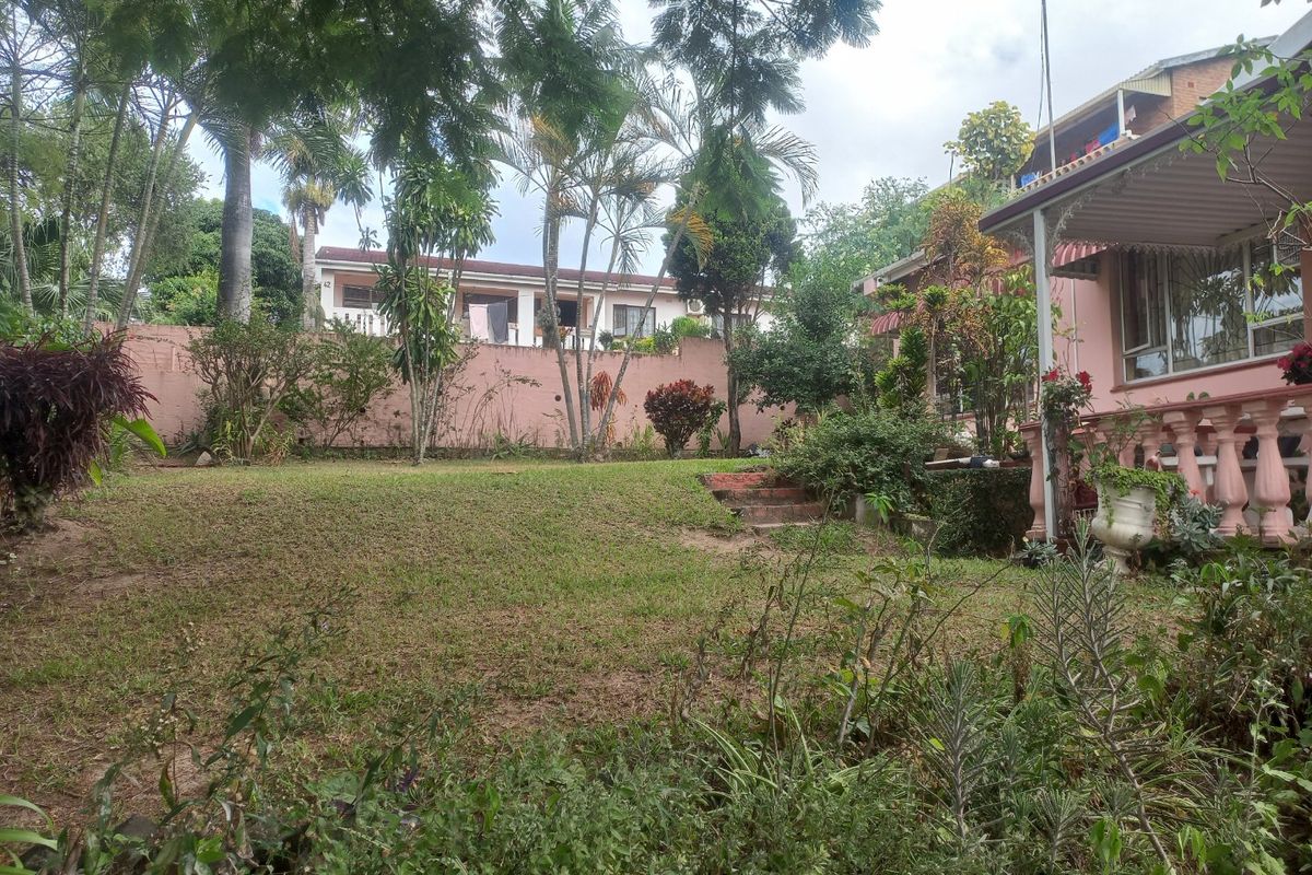 A rear garden view featuring a lawn area, boundary wall, and a covered patio with a decorative concrete balustrade.