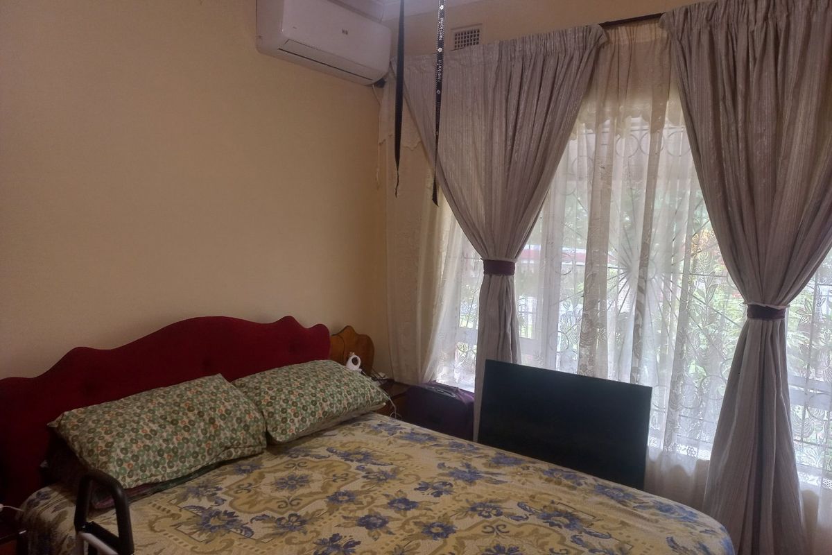 A bedroom featuring a wall-mounted split-system air conditioner and large window with security gate, providing natural light and climate control.