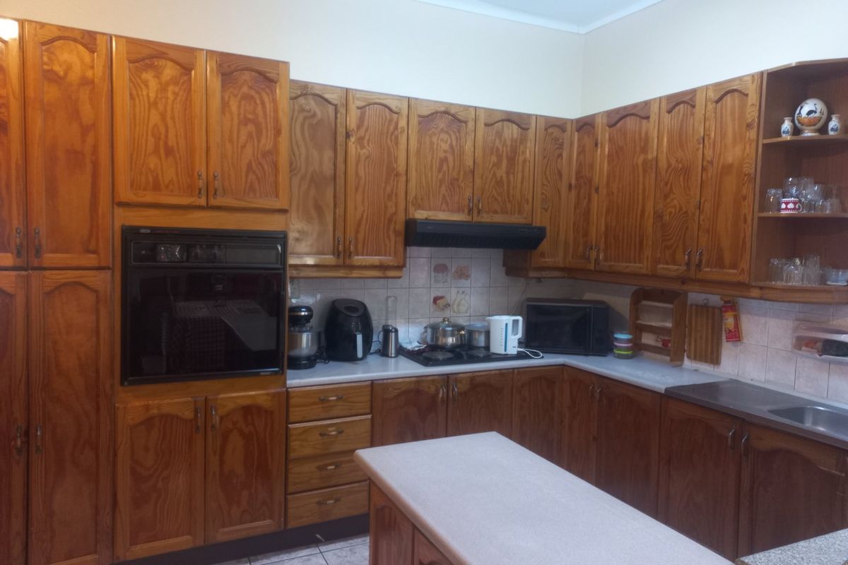 A functional kitchen featuring extensive wooden cabinetry, built-in oven, extractor fan, and tiled finishes, offering a traditional layout with ample storage space.